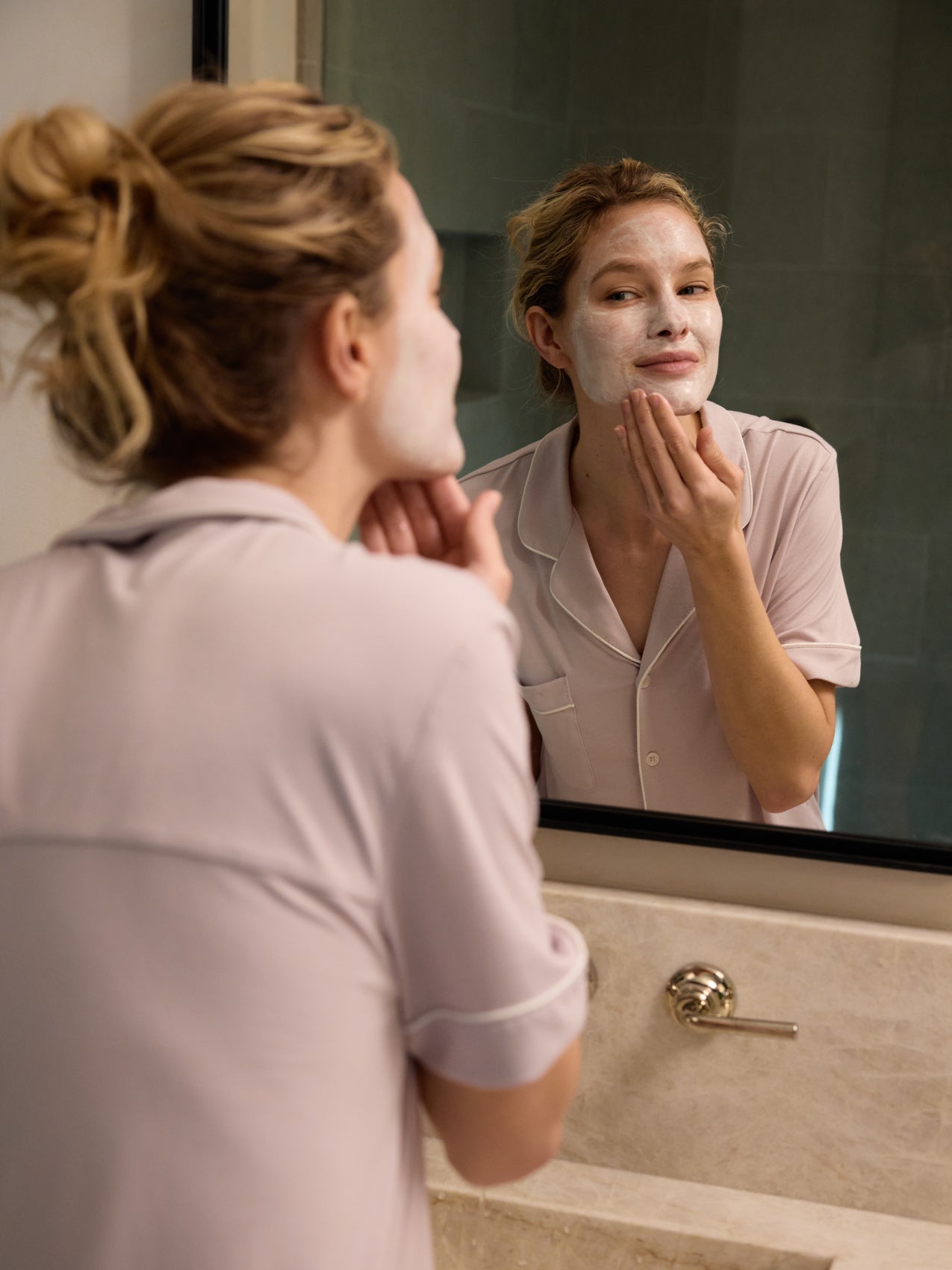 A woman applies Fount Society Clay Mask to her entire face in a bathroom mirror. |Size:Mini