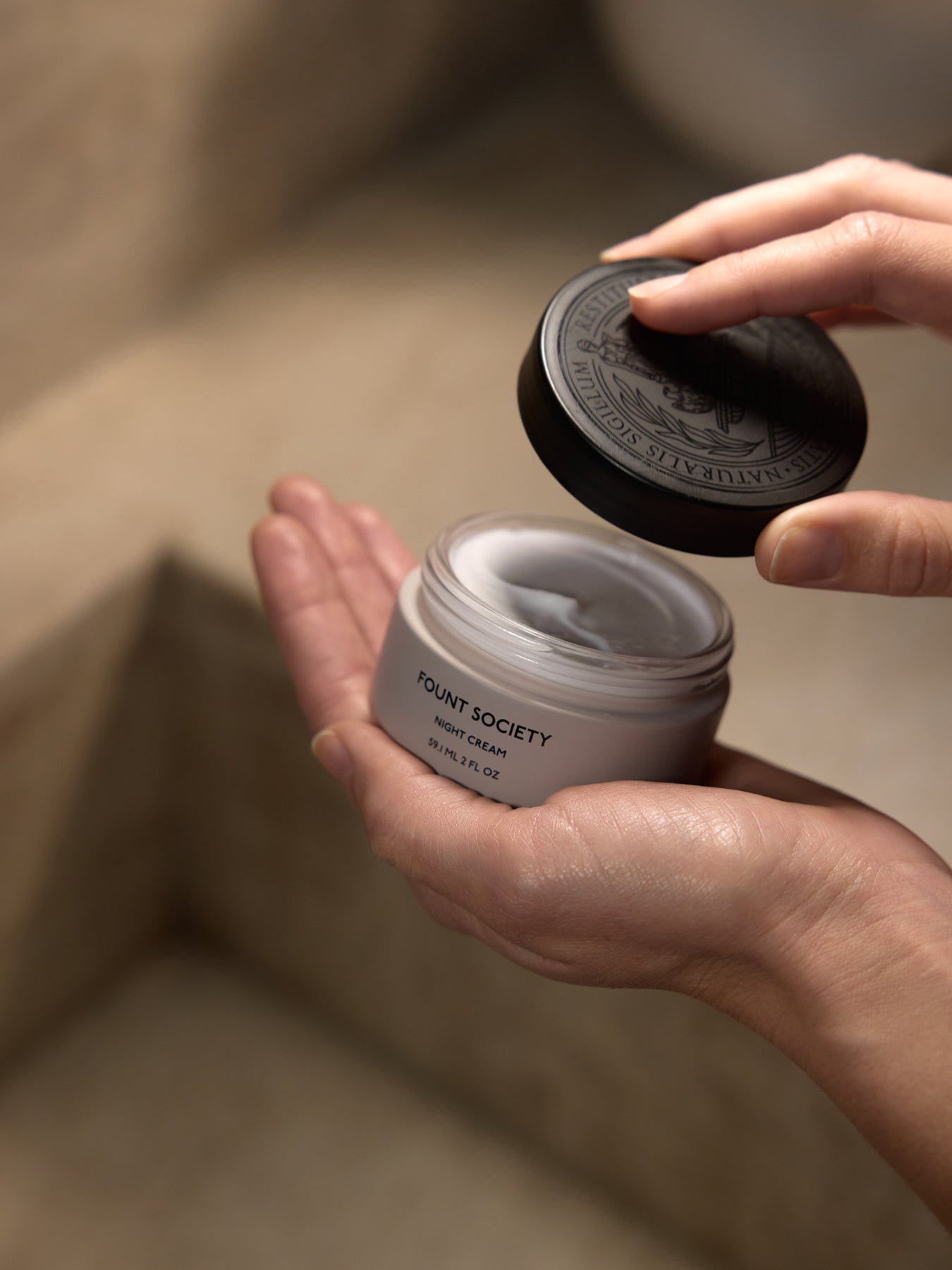 A woman holds an open container of Fount Society Night Cream. |Size:Full Size